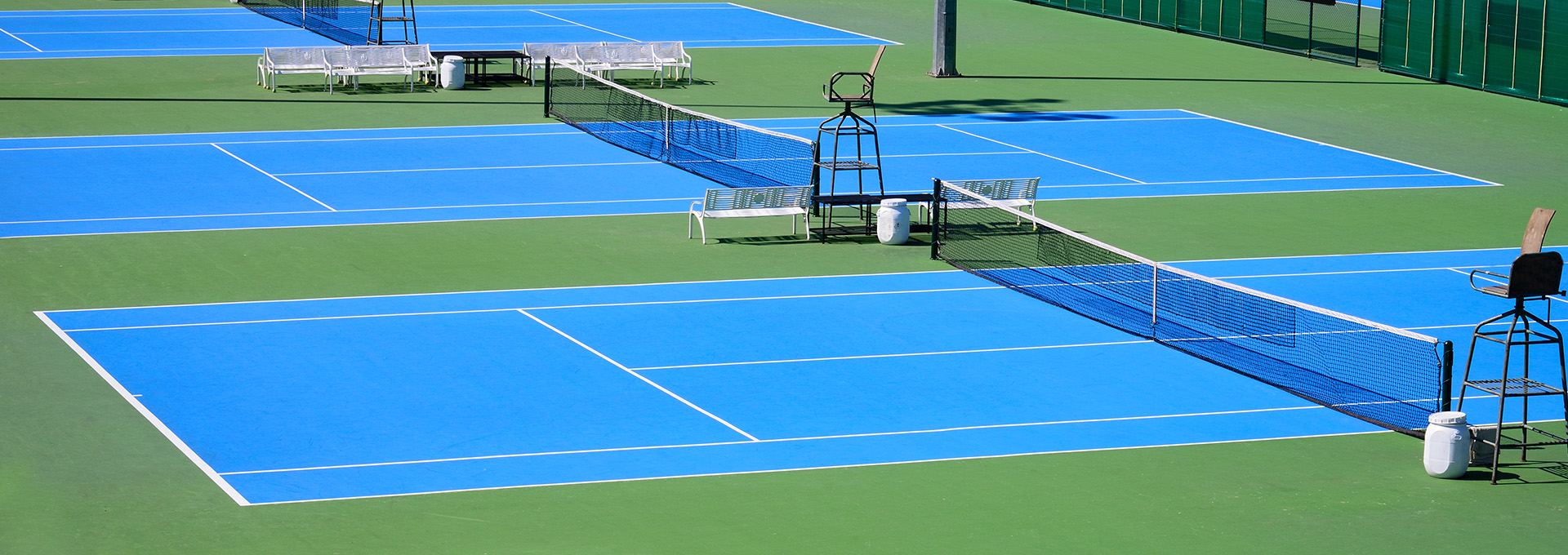 Multiple blue outdoor tennis courts with green surroundings
