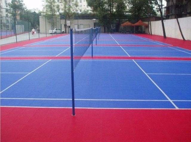 Outdoor volleyball court with blue surface, red end zones, and volleyball net