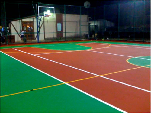 Outdoor multi-sport court at night with green volleyball area and orange basketball area